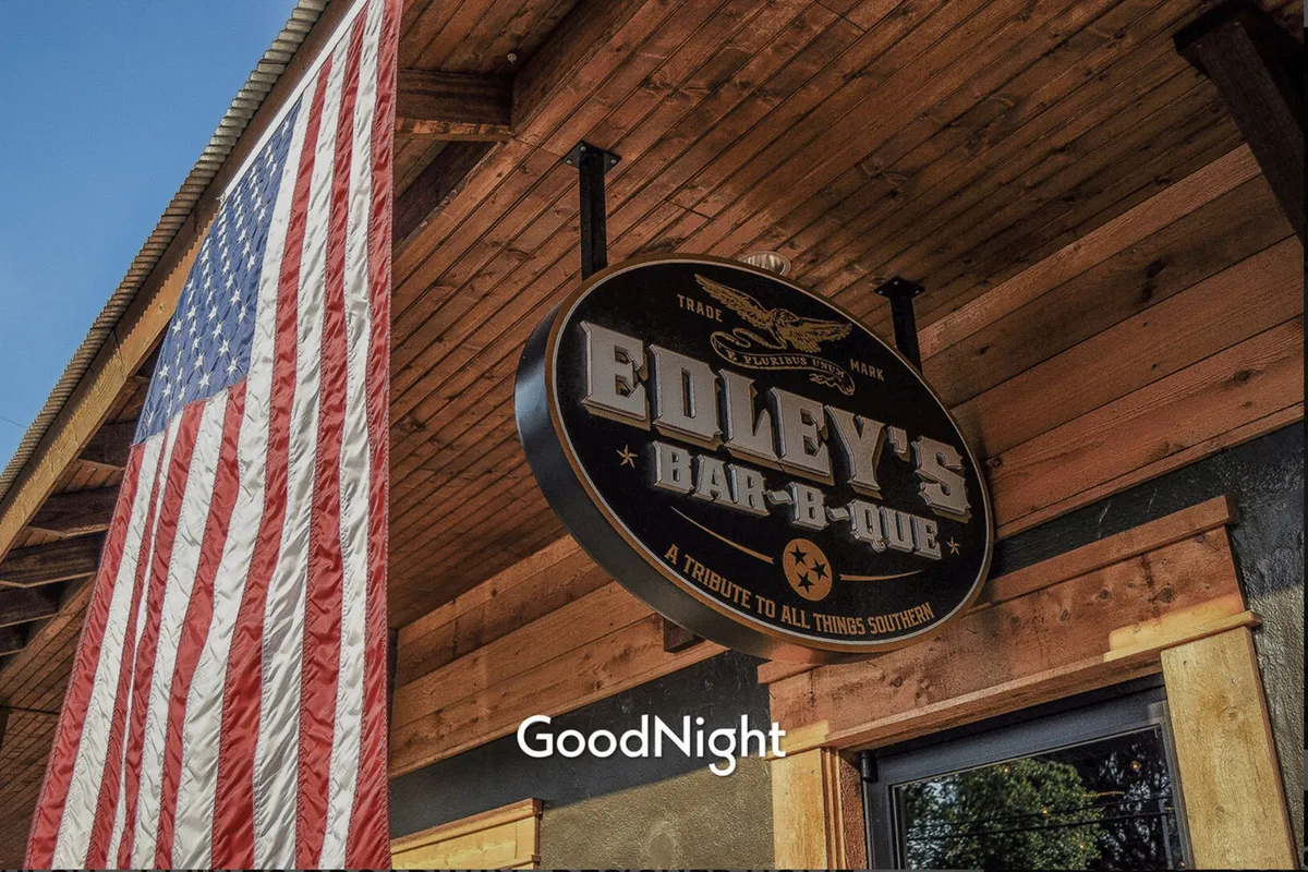 An exterior shot featuring an American flag and a restaurant sign, capturing the welcoming and social atmosphere of a local Nashville eatery. The outdoor setting hints at neighborhood amenities and community events, connecting guests to the surrounding area.