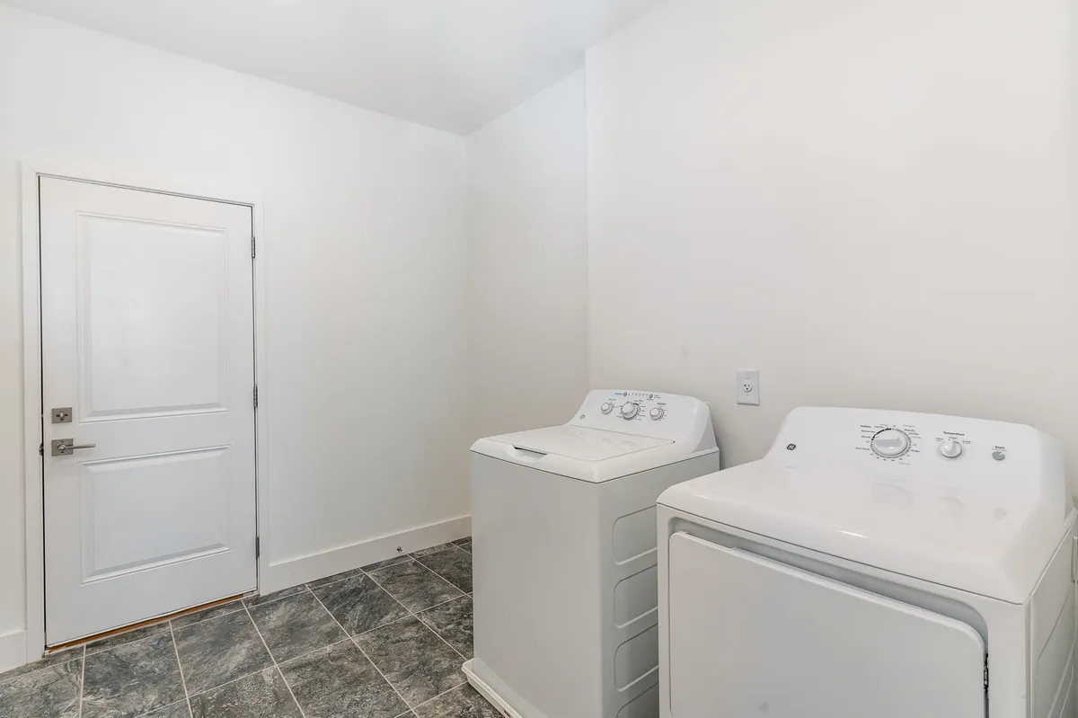 A compact yet functional laundry space featuring a washer and dryer, with a door leading to adjacent areas. The setup is clean and organized, underscoring the convenience of in-home laundry facilities.