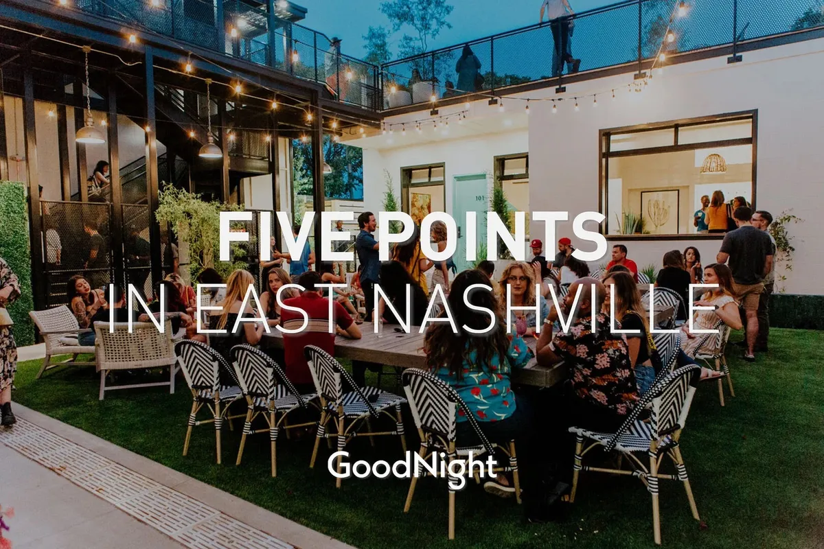 A lively outdoor scene featuring a large group of people gathered in a modern exterior seating area, illuminated by decorative lighting. The architecture is sleek, and the atmosphere suggests active socializing, dining, and celebration.