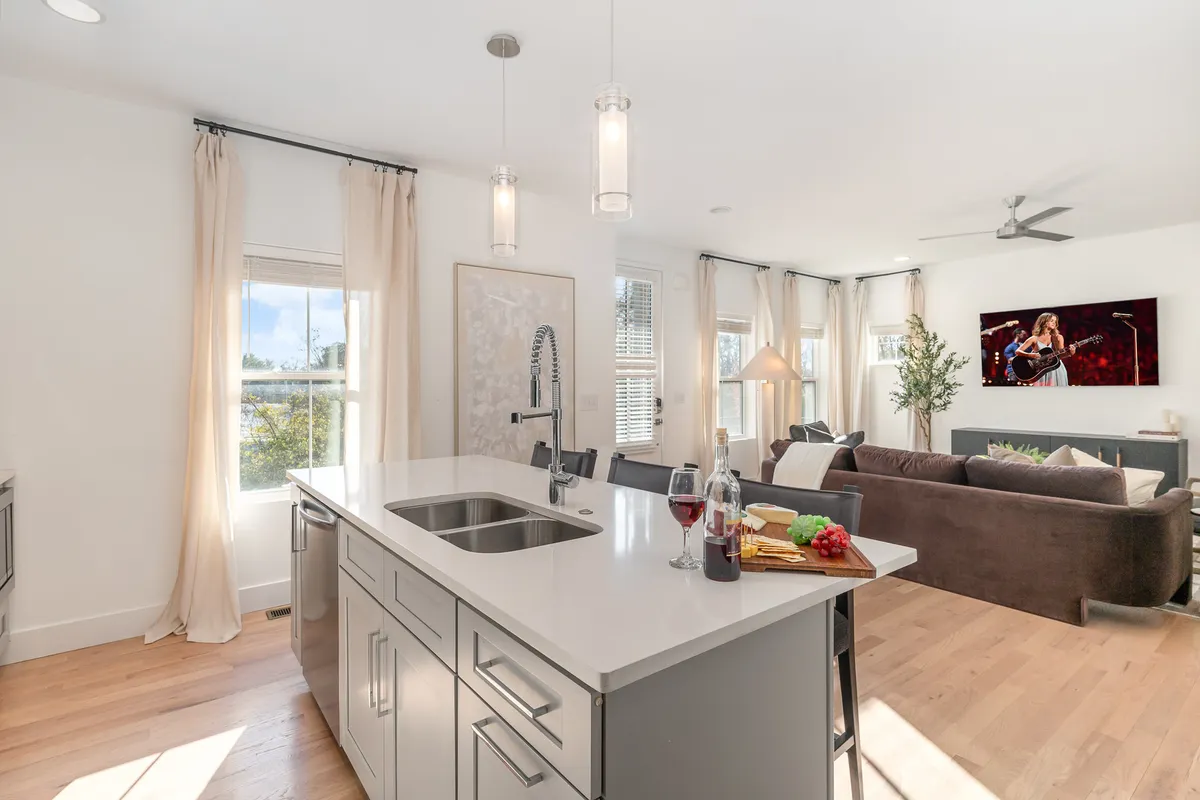 An open-concept space combining a kitchen island, living room seating, television, and large windows. The arrangement allows for seamless transitions between cooking, entertaining, and relaxing.
