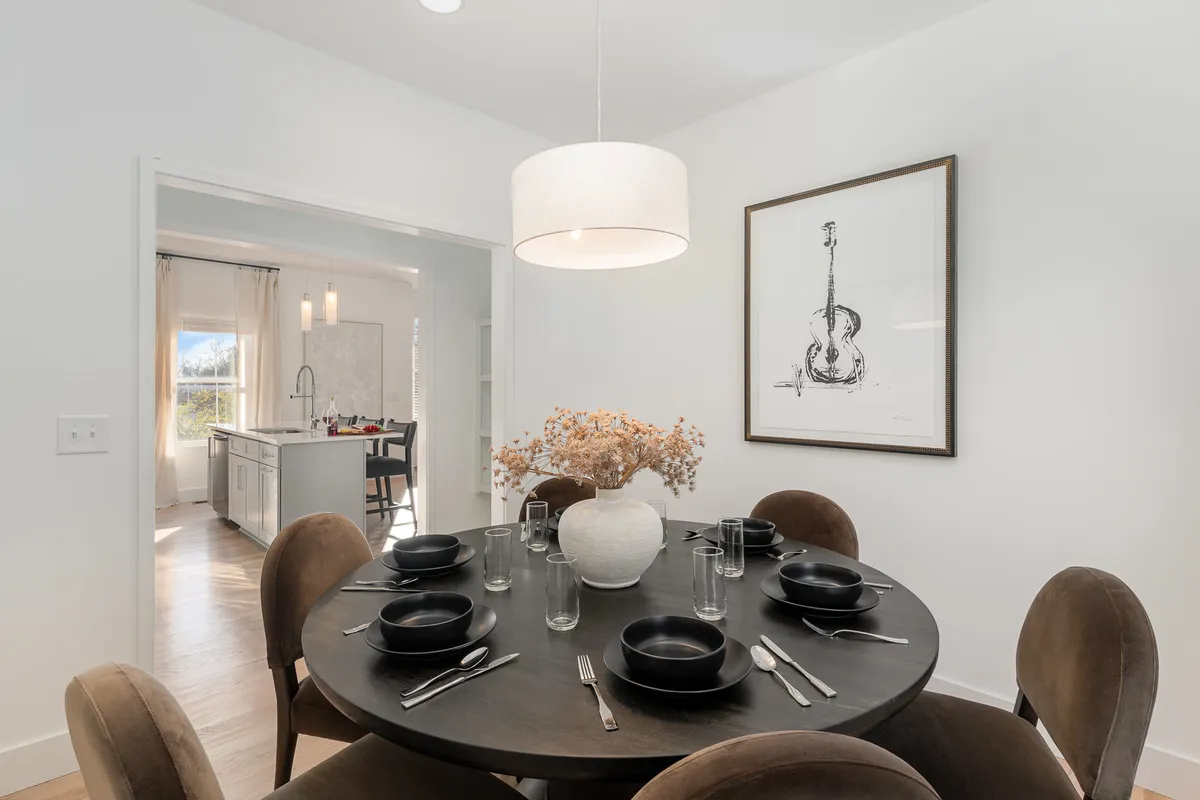 A round dining table with a central vase of dried flowers sits beneath guitar-themed artwork, creating a warm and artistic dining area ideal for shared family meals or social gatherings.
