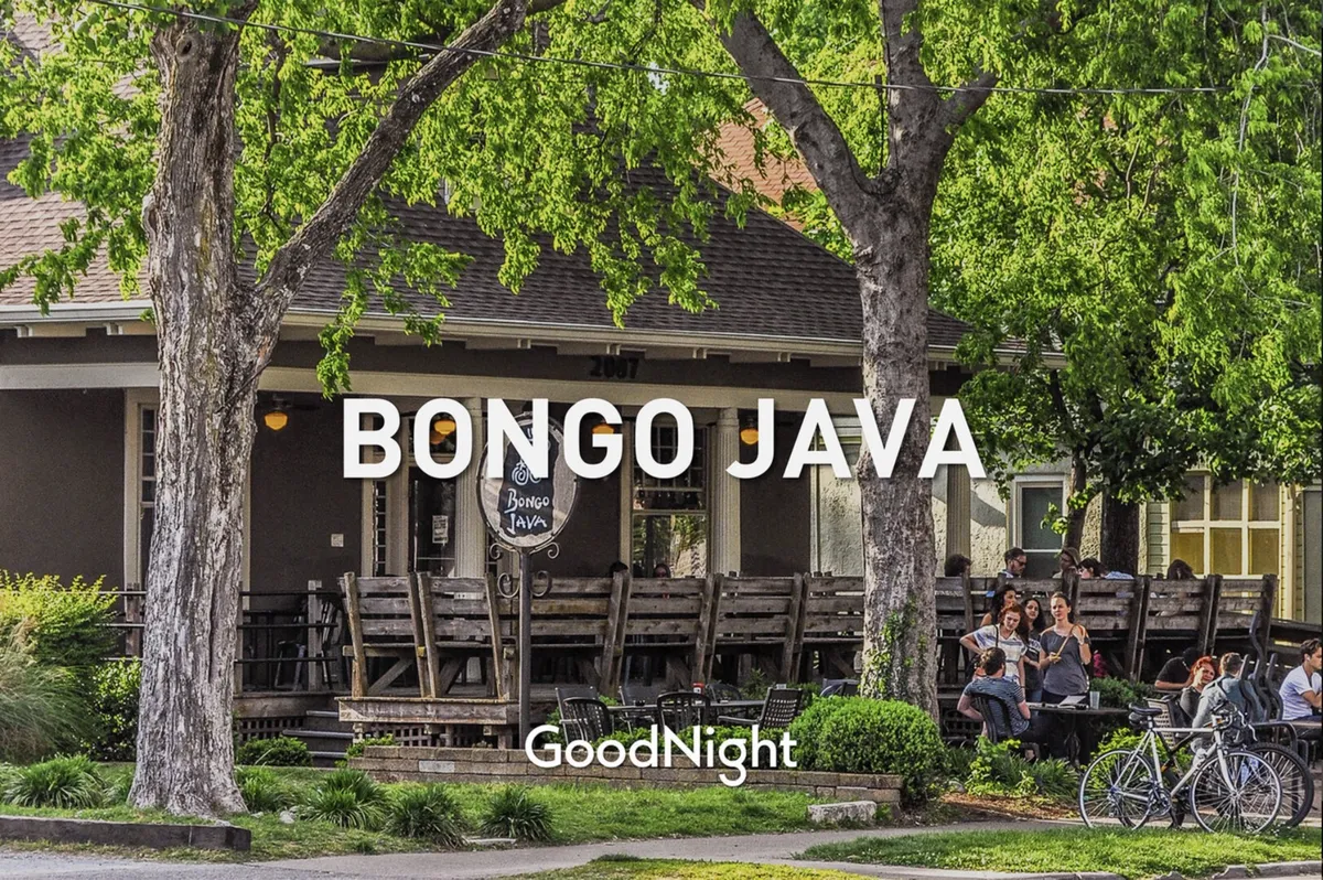 A lively exterior scene of a coffee shop with outdoor seating, people socializing, and bicycles parked nearby. The bright, friendly atmosphere suggests a convenient spot for morning routines or casual meetups close to the property.