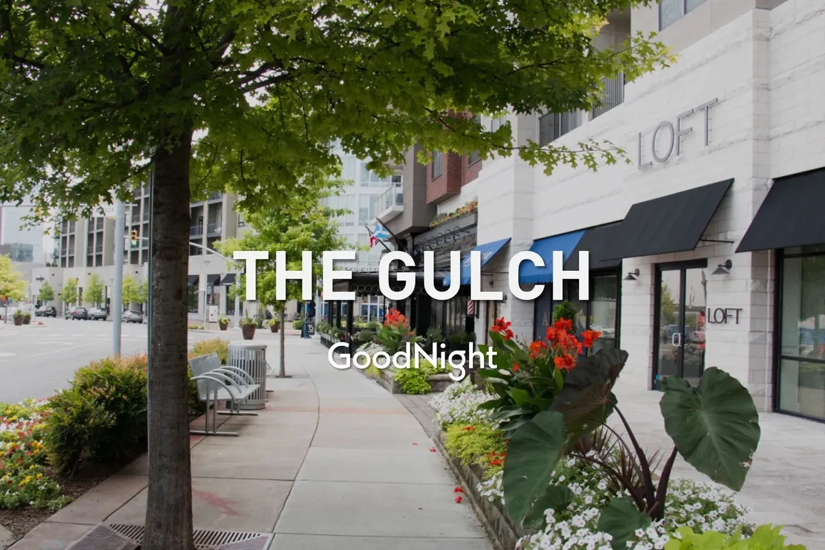 A vibrant outdoor scene featuring well-maintained flower beds, benches, and trees, providing a sense of a lively and welcoming neighborhood. The inviting atmosphere encourages outdoor relaxation and socializing under sunny skies.