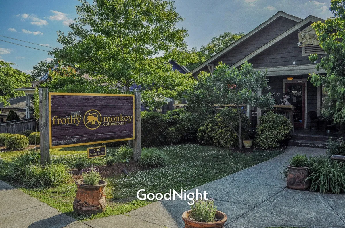 A welcoming coffeehouse storefront with a sign for Frothy Monkey, a landscaped garden, and a cozy front porch. The setting is relaxed and inviting, perfect for enjoying coffee or community gatherings.