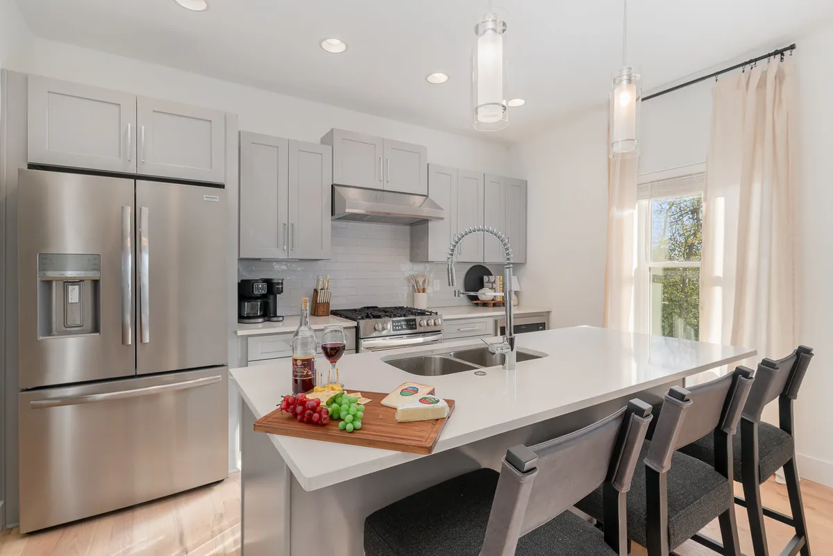 A stylish kitchen with a prominent island, gleaming stainless steel appliances, and elegant finishes. The setup includes a fruit platter and wine glasses, suggesting readiness for entertaining or family meals. The ample counter space and inviting mood reinforce the kitchen’s role as both a functional and social hub.